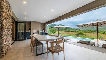 A modern outdoor dining area with a stone wall, a pool, and a view of the countryside.