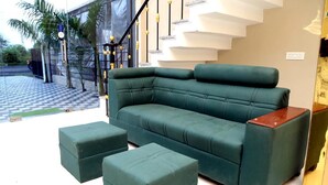 En moderne stue med en grøn sofa og matchende skottomaner, en trappe med et unikt design, og udsigt udad.
