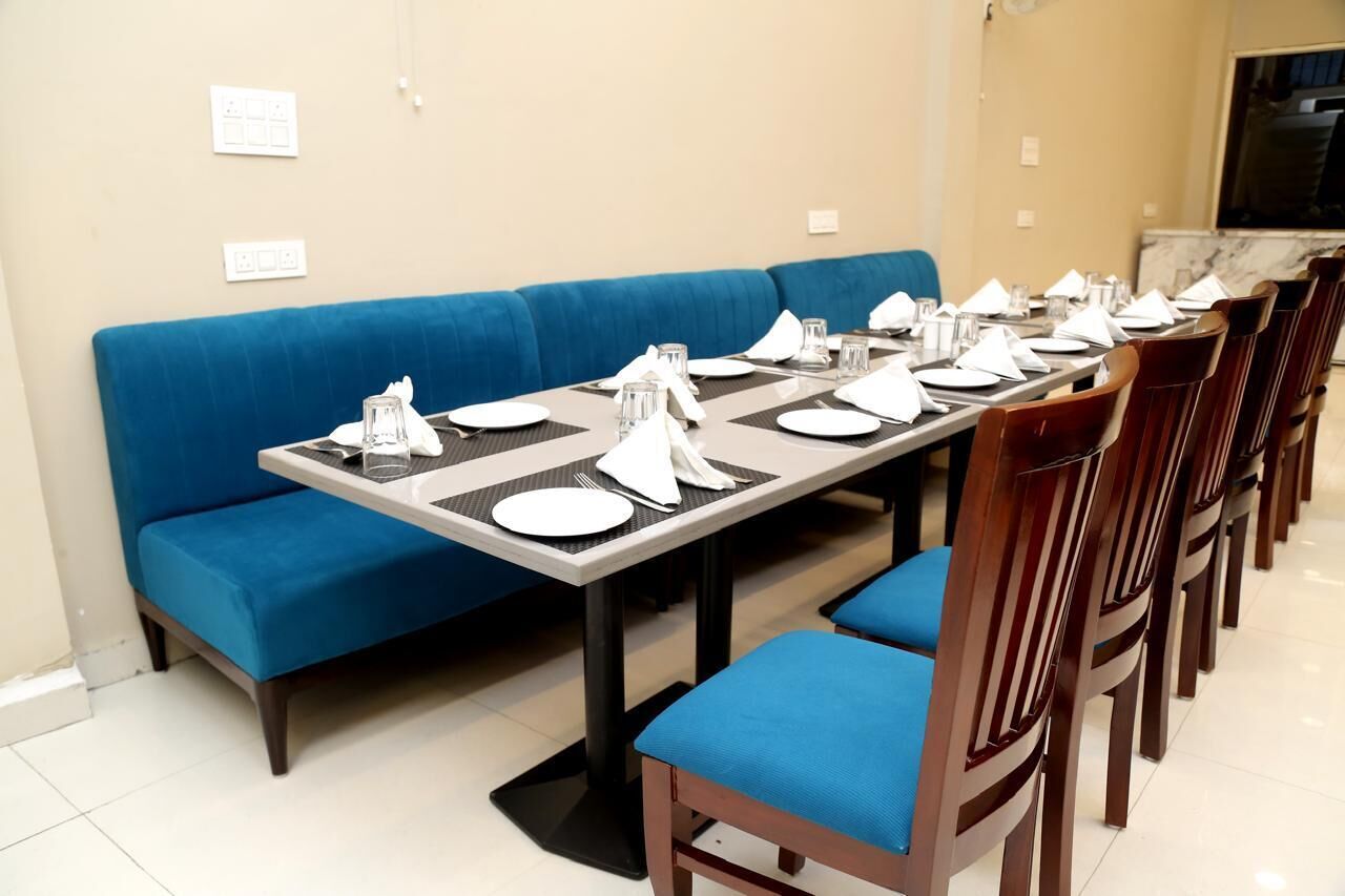 A dining area with a long table set for multiple guests, blue cushioned seating, and a marble countertop in the background.