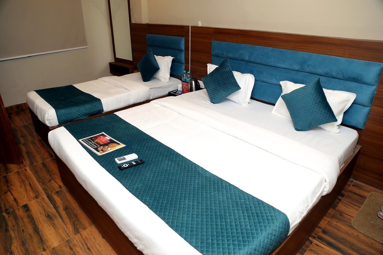 Une chambre d’hôtel avec deux lits simples, chacun doté d’une tête de lit bleue et de draps blancs. Un plaid turquoise est posé sur le plus grand lit, et une télécommande et un magazine se trouvent sur le plus petit lit.