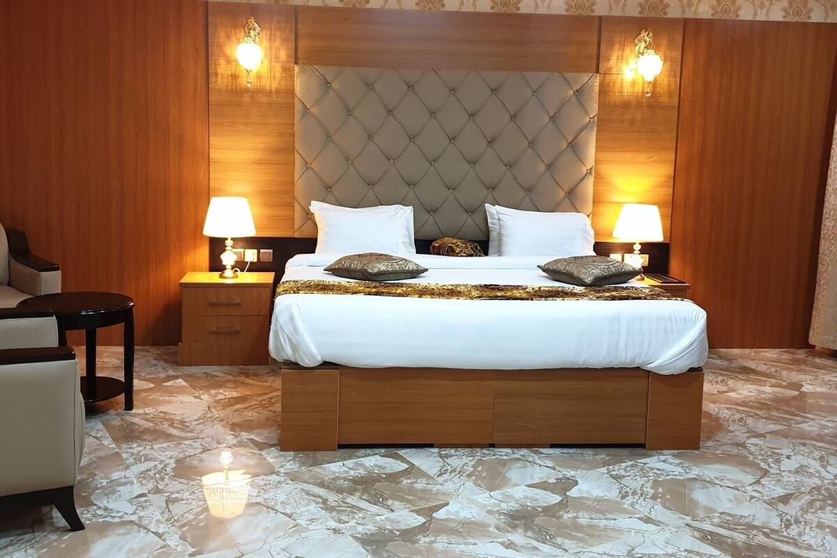 Une chambre spacieuse avec un grand lit, deux tables de chevet avec des lampes, une tête de lit en bois et un papier peint à motifs.