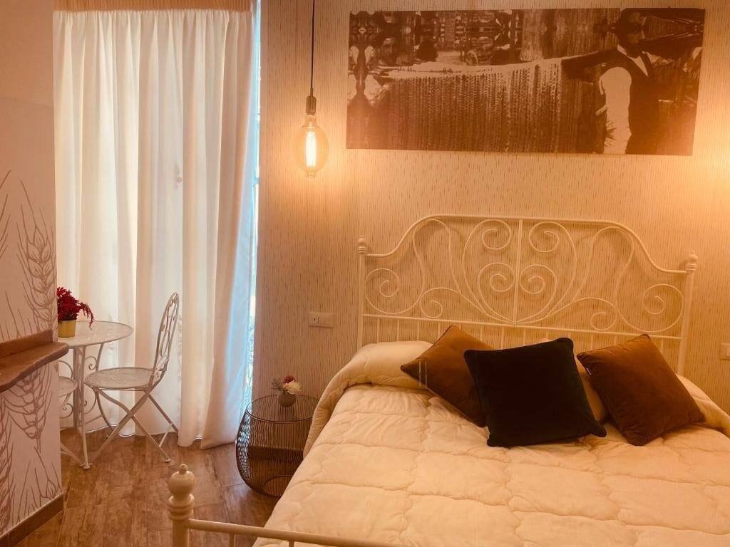 A bedroom with a bed, a chair, a table, and a hanging light bulb.