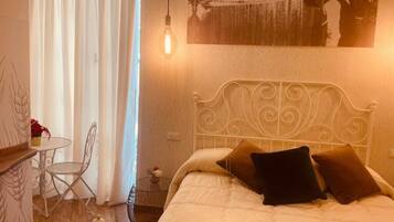 A bedroom with a bed, a chair, a table, and a hanging light bulb.
