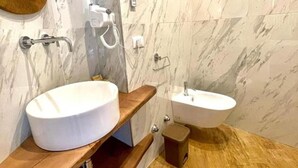 A bathroom with two sinks, marble walls, wooden shelves, and a small trash bin. - GRANORO B&B (Gragnano)