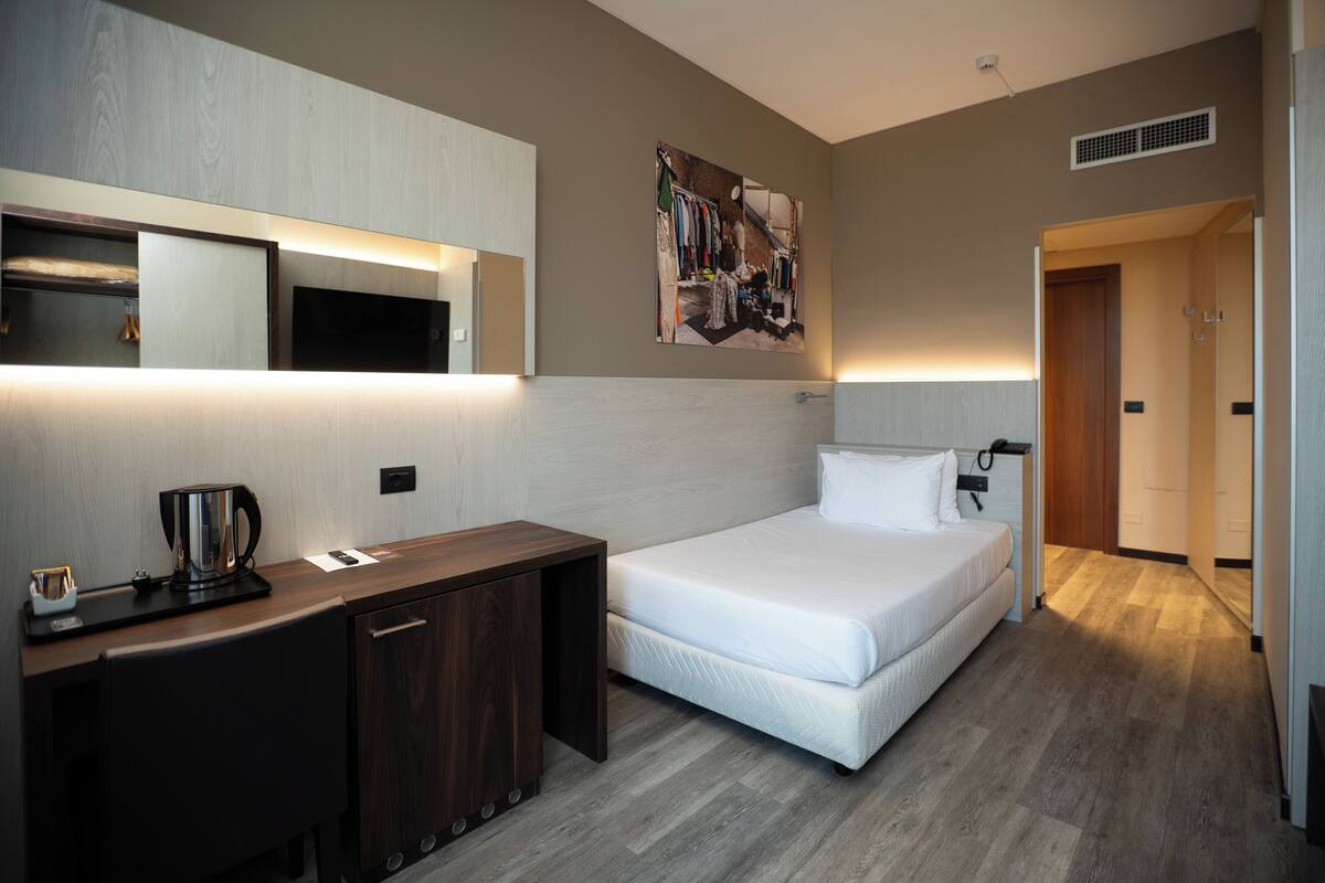 Una habitación de hotel con cama, mesita de noche y escritorio con cafetera.