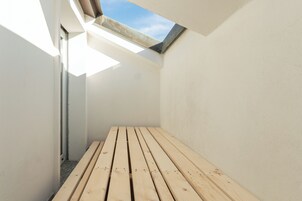 Una habitación estrecha, iluminada por el sol, con un banco de madera y un tragaluz.