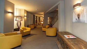 Un hall de hotel con varios sillones amarillos, un mostrador de recepción de madera y una escalera que conduce a otro piso.