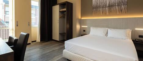 A hotel room with a large bed, a desk, and a wardrobe.