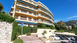 Un hotel de varios pisos con balcones, un estacionamiento y un cielo azul despejado.