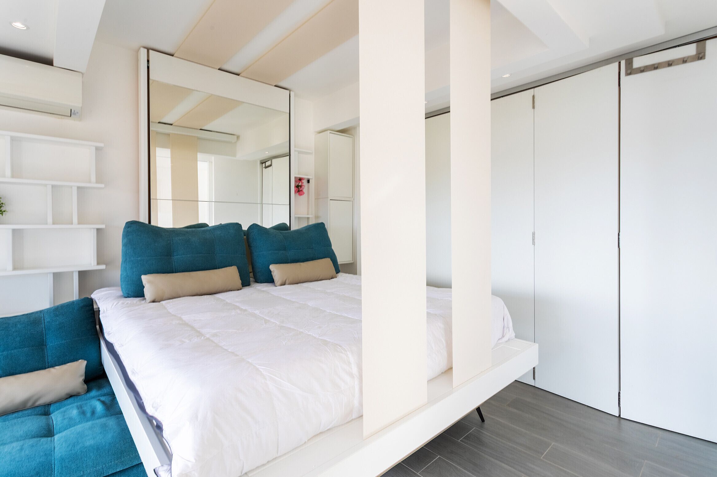 A modern bedroom with a large bed, white walls, and a built-in wardrobe.
