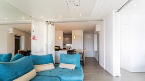 Una sala de estar moderna con un sofá seccional azul, una cocina al fondo y un pasillo que conduce a una puerta.