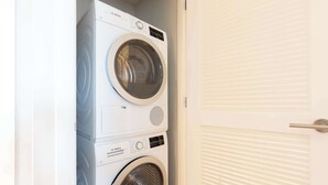 A stacked washer and dryer unit in a laundry room with a white door. - Luxury Apt In Heart of Seaport (Boston MA)