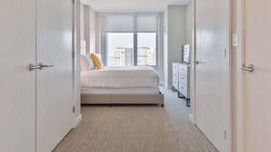 A modern hotel room with a large bed, a dresser, and a view of the city through the window. - Luxury Apt In Heart of Seaport (Boston MA)