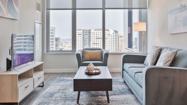 A modern living room with a large window, a flat-screen TV, a coffee table, and a sofa. - Luxury Apt In Heart of Seaport (Boston MA)