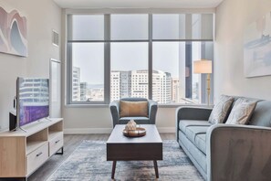 A modern living room with a large window, a flat-screen TV, a coffee table, and a sofa. - Luxury Apt In Heart of Seaport (Boston MA)