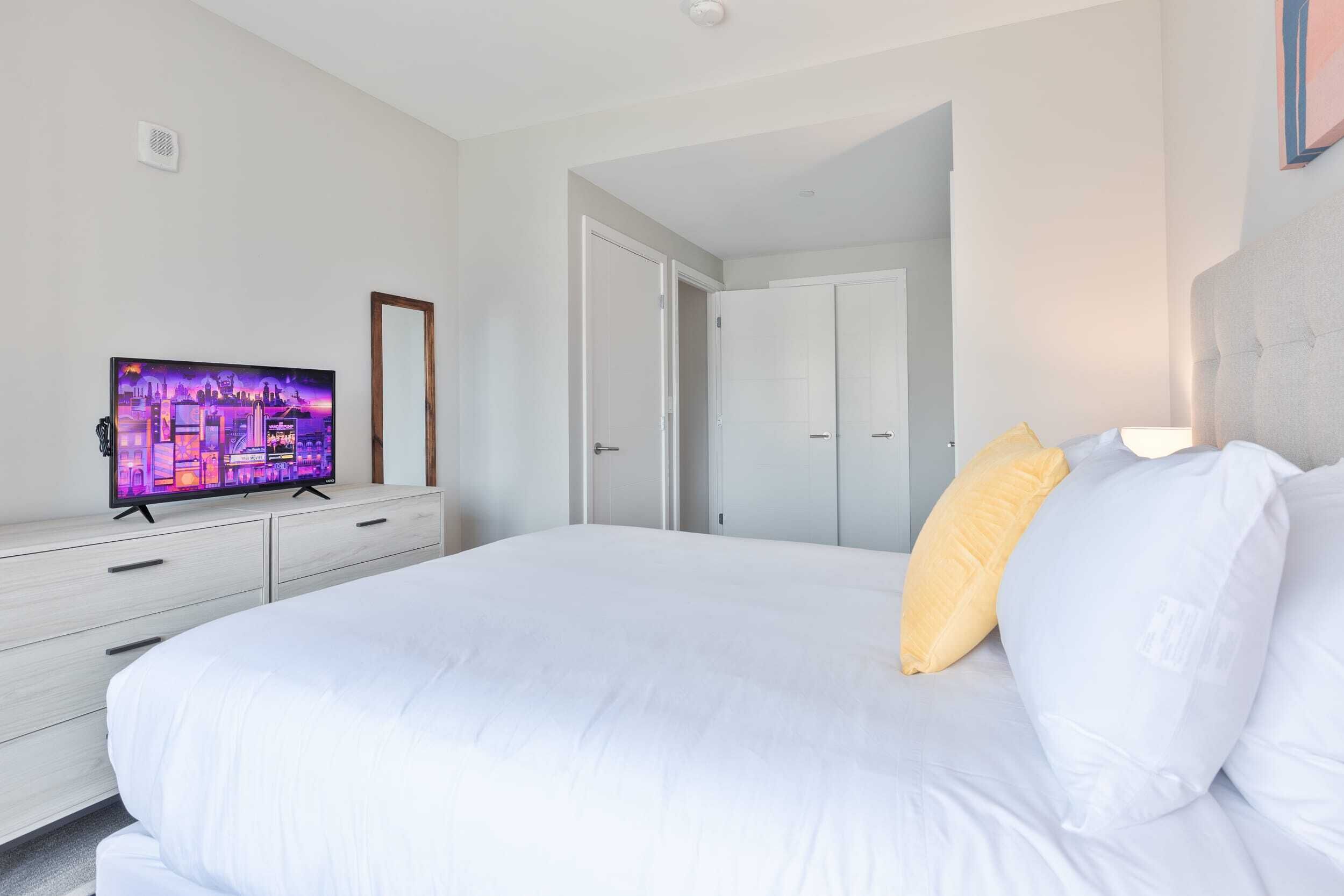 A bedroom with a bed, a TV on a dresser, and a door leading to another room.
