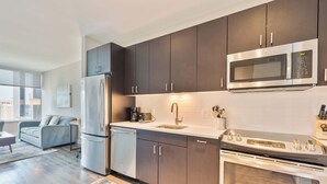 A modern kitchen with dark cabinets, stainless steel appliances, and a large window. - Luxury Apt In Heart of Seaport (Boston MA)