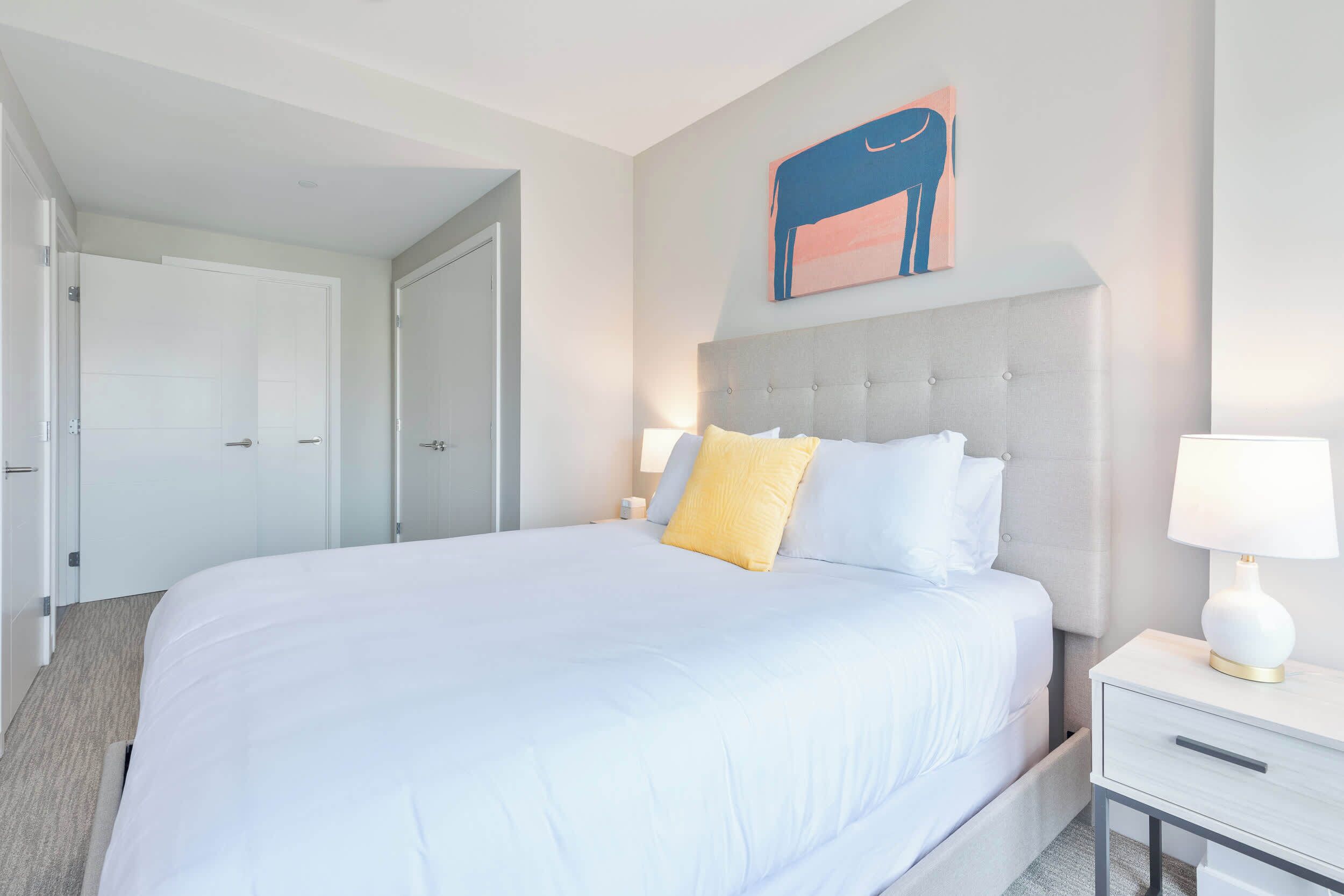A hotel room with a large bed, a bedside table with a lamp, and a door leading to another room.