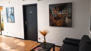 Eine Hotelhalle mit Holzboden, einer schwarzen Couch, einem schwarzen Tisch mit Zeitschriften, einer Vase mit Trockenpflanzen und einem Gemälde einer Gitarre.