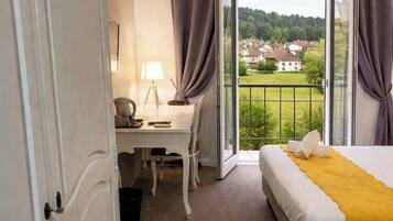 Een hotelkamer met een bed, een bureau, een stoel, een lamp en uitzicht op een groen landschap door een glazen deur.