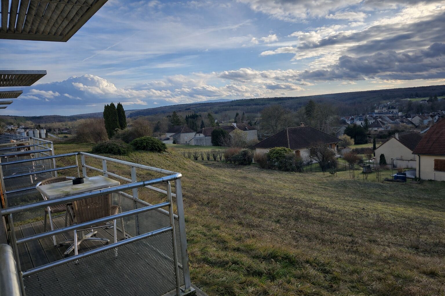 Uitzicht vanaf een balkon op een woonwijk met huizen, een grasveld en een bewolkte lucht.