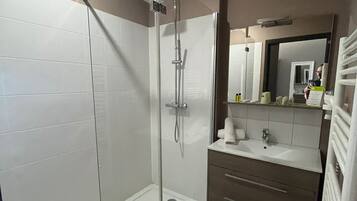 Un baño moderno con ducha de vidrio, tocador con espejo y inodoro.