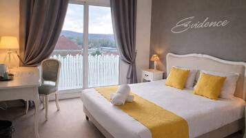 Habitación de hotel con cama, escritorio, silla, mesita de noche y vistas al exterior.