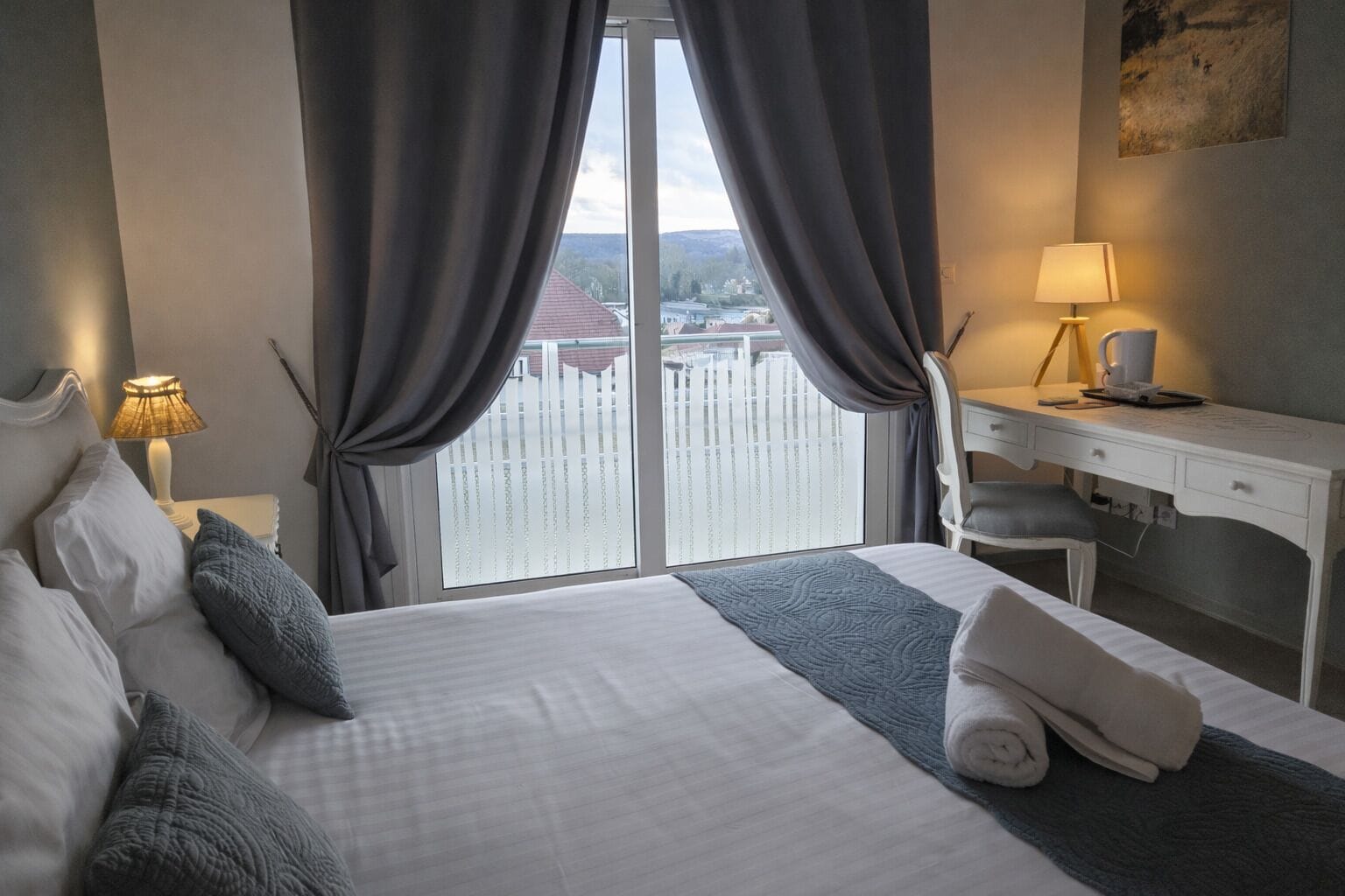 Une chambre d’hôtel avec un lit, un bureau, une chaise, une lampe et une vue sur une étendue d’eau par la fenêtre.
