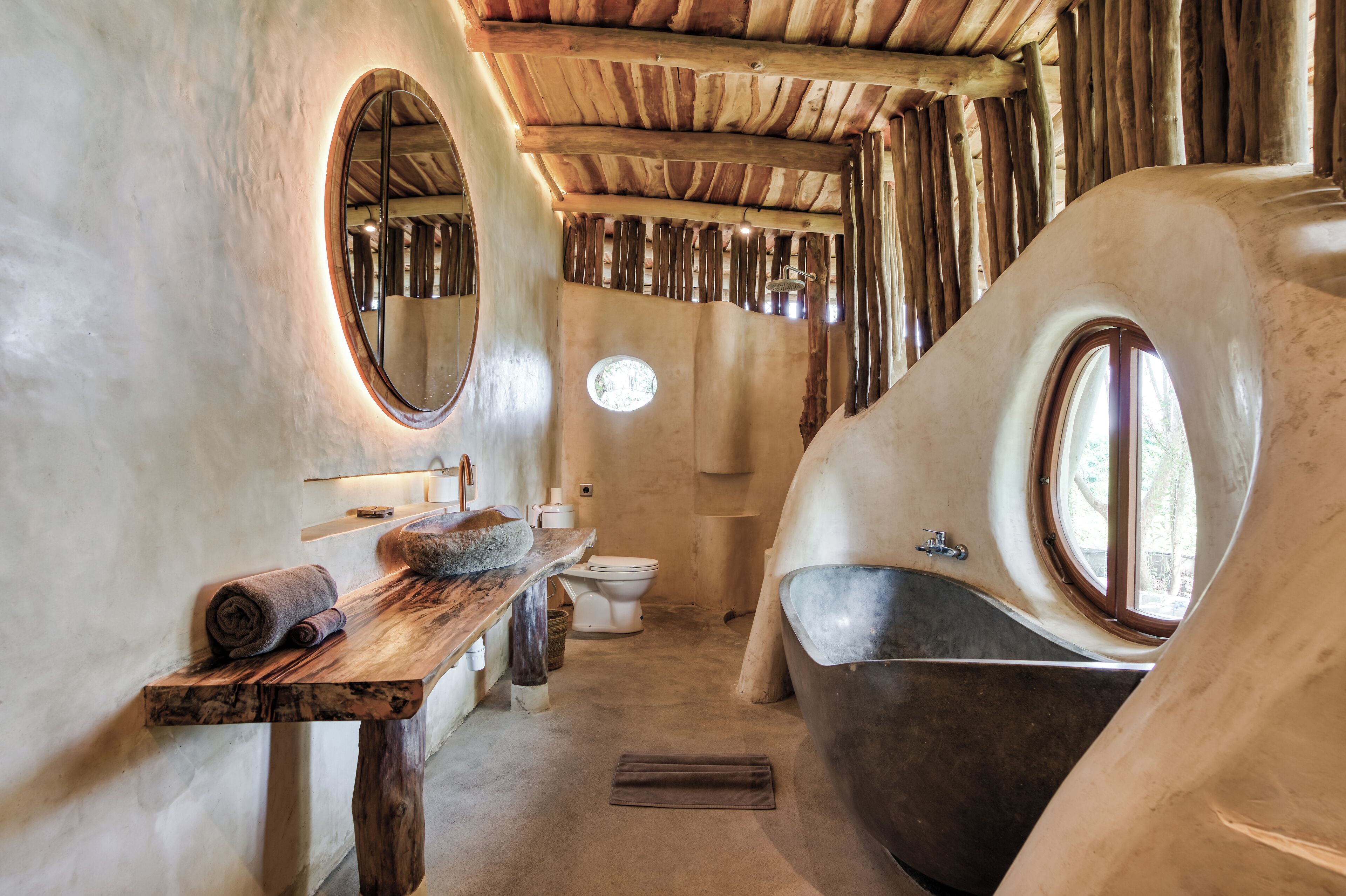 A bathroom with a wooden vanity, a round mirror, and a large bathtub.
