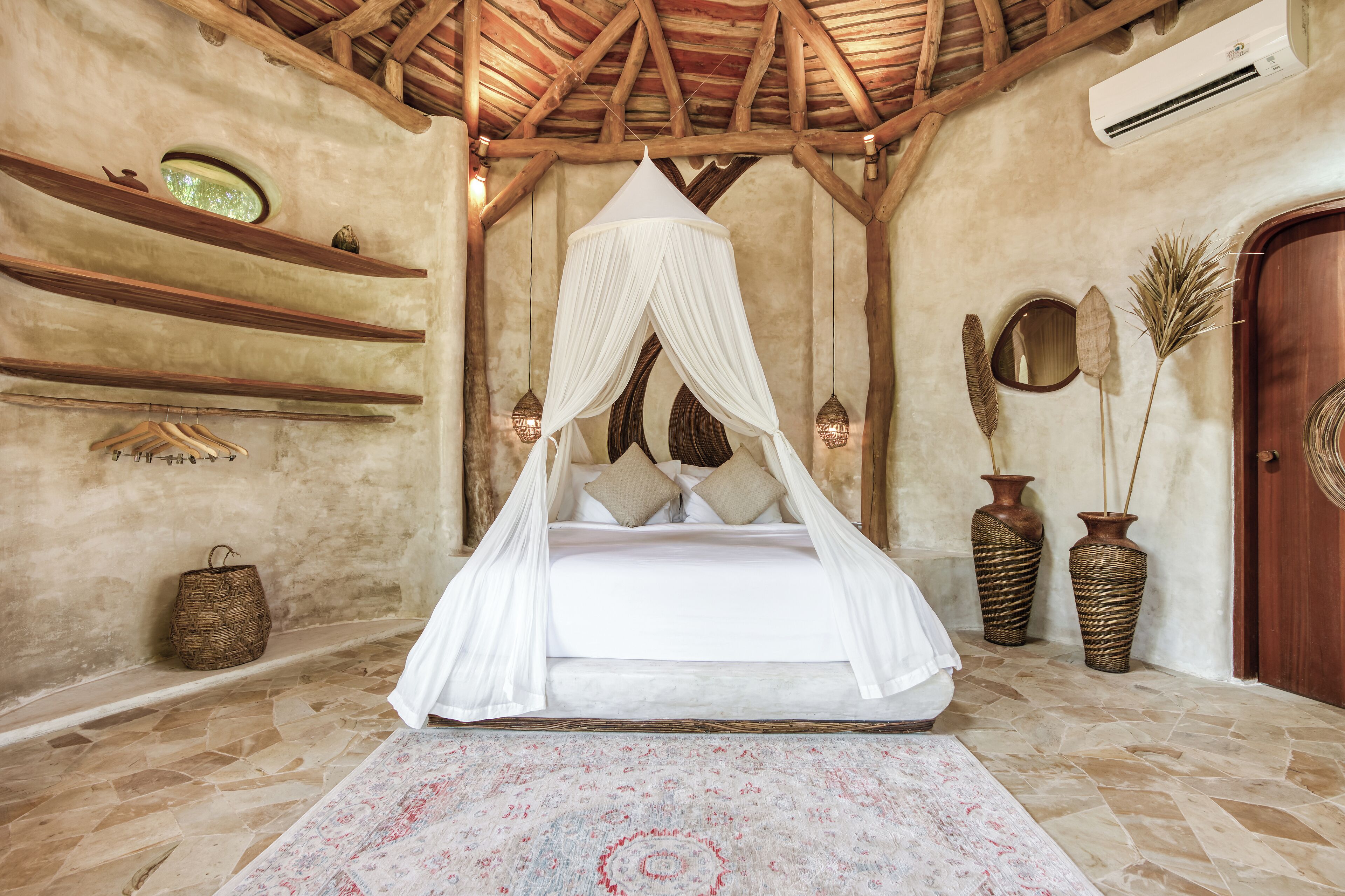 Un dormitorio con cama a dosel, paredes de piedra, vigas de madera, una cesta tejida y dos jarrones.