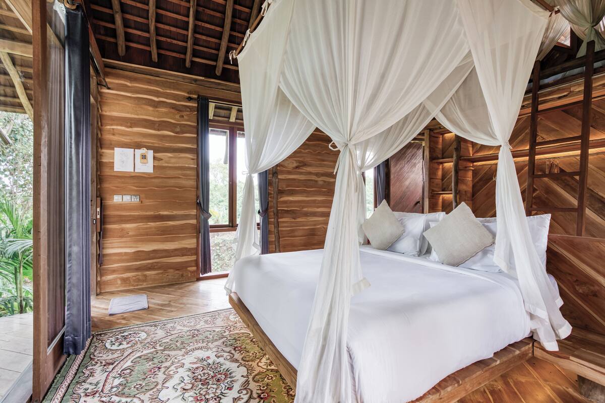 A wooden room with a bed, a large window, and a door.