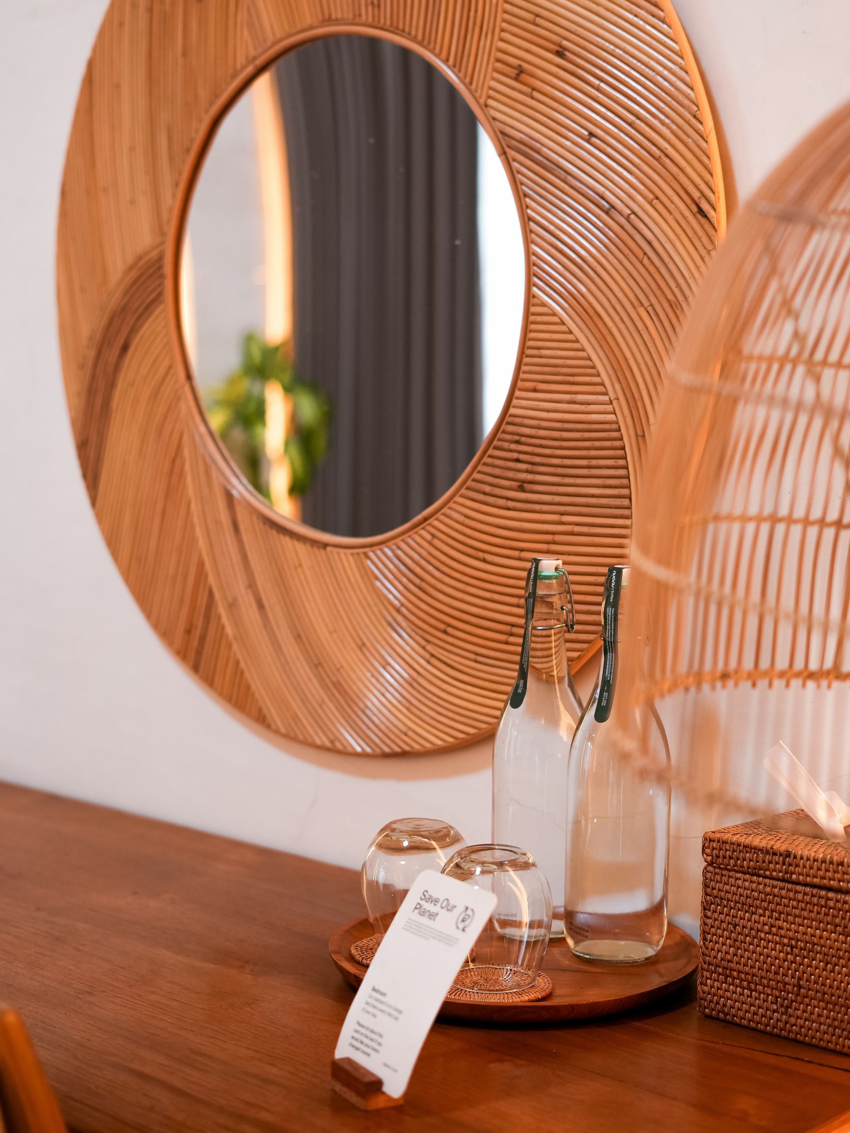 A wooden table with a round mirror, a glass bottle, and a wicker basket.