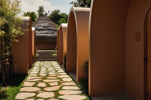 Un sendero conduce a un edificio de techo de paja, rodeado de follaje y un camino de losas de piedra.
