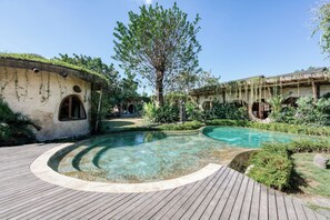 A pool area with a wooden deck, surrounded by lush greenery and traditional architecture. - Nuanu Suites & Accommodations (Tabanan)