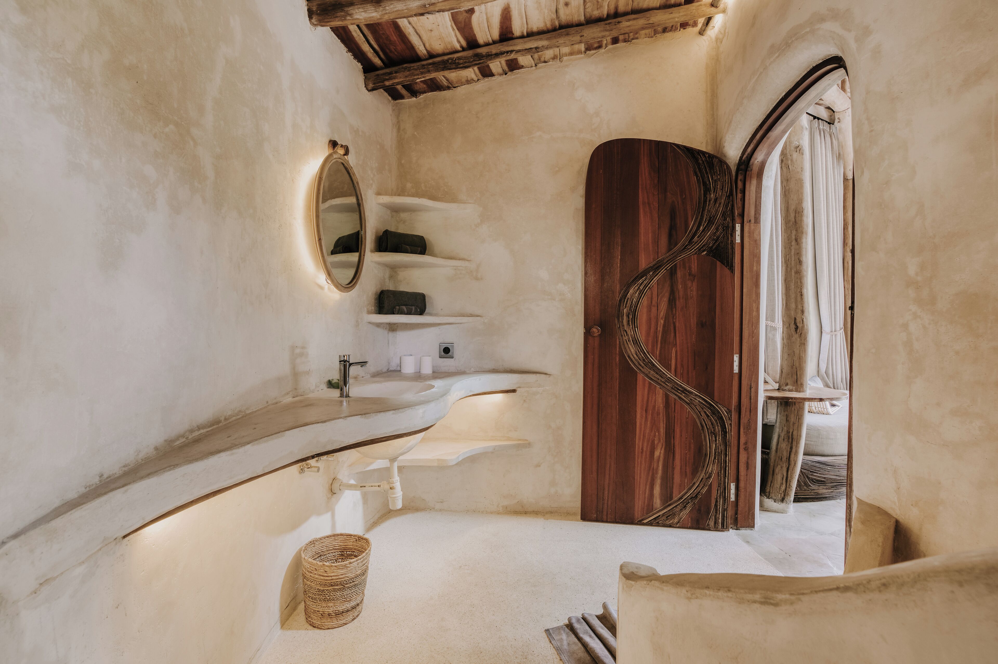 A bathroom with a curved sink, a wooden door, and a mirror.