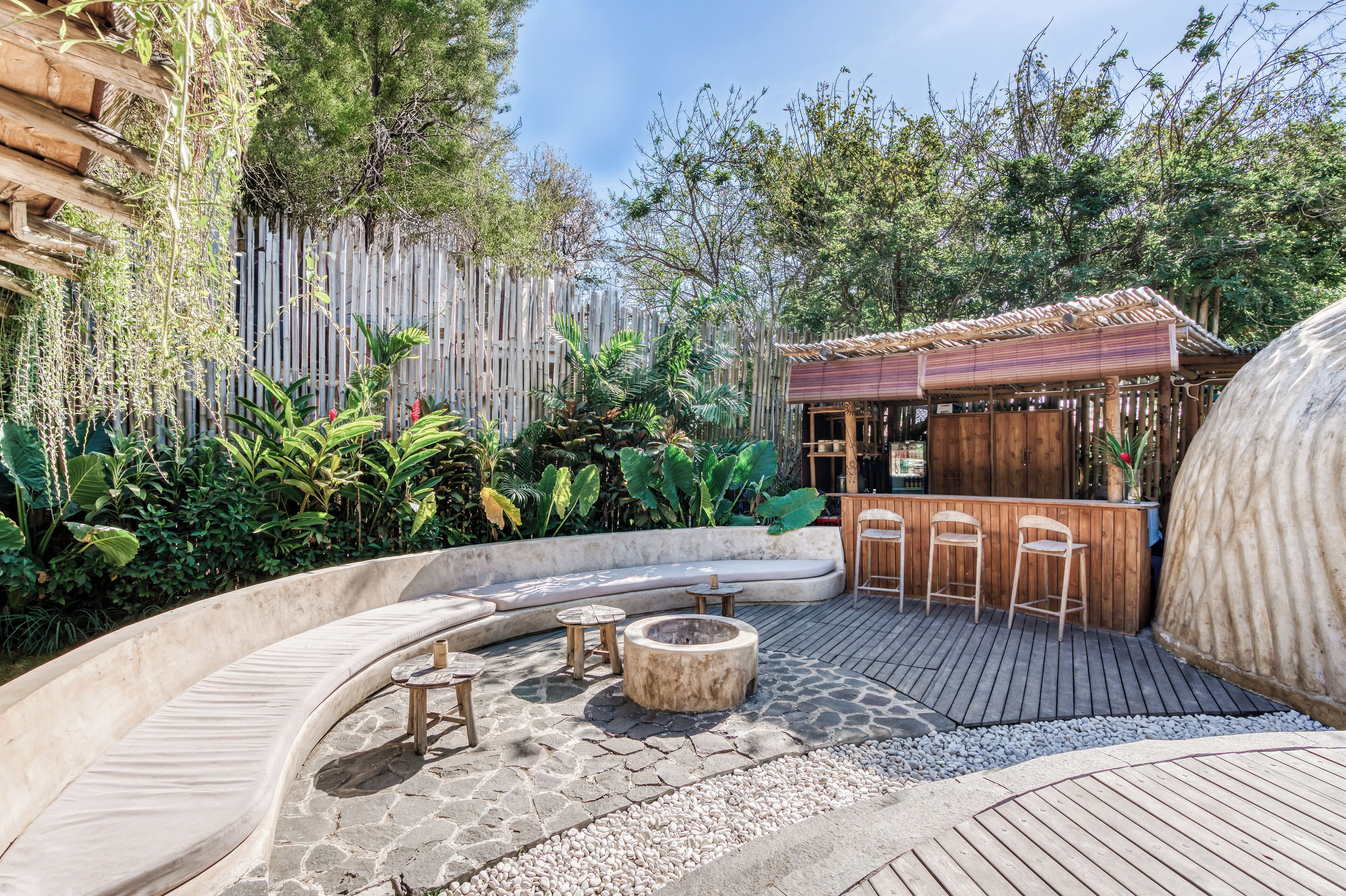 A curved outdoor seating area with a fire pit, wooden tables, and a bar area with stools.