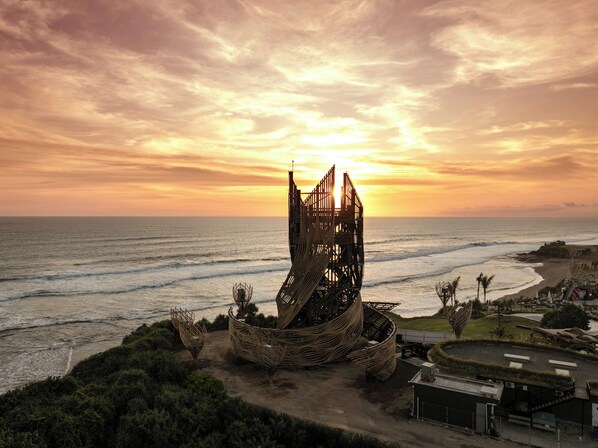 Vista costera con una escultura moderna y singular junto al mar al atardecer.