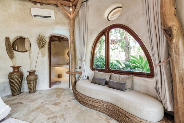 A cozy room with a curved sofa, large windows, and rustic decor. - Nuanu Suites & Accommodations (Tabanan)