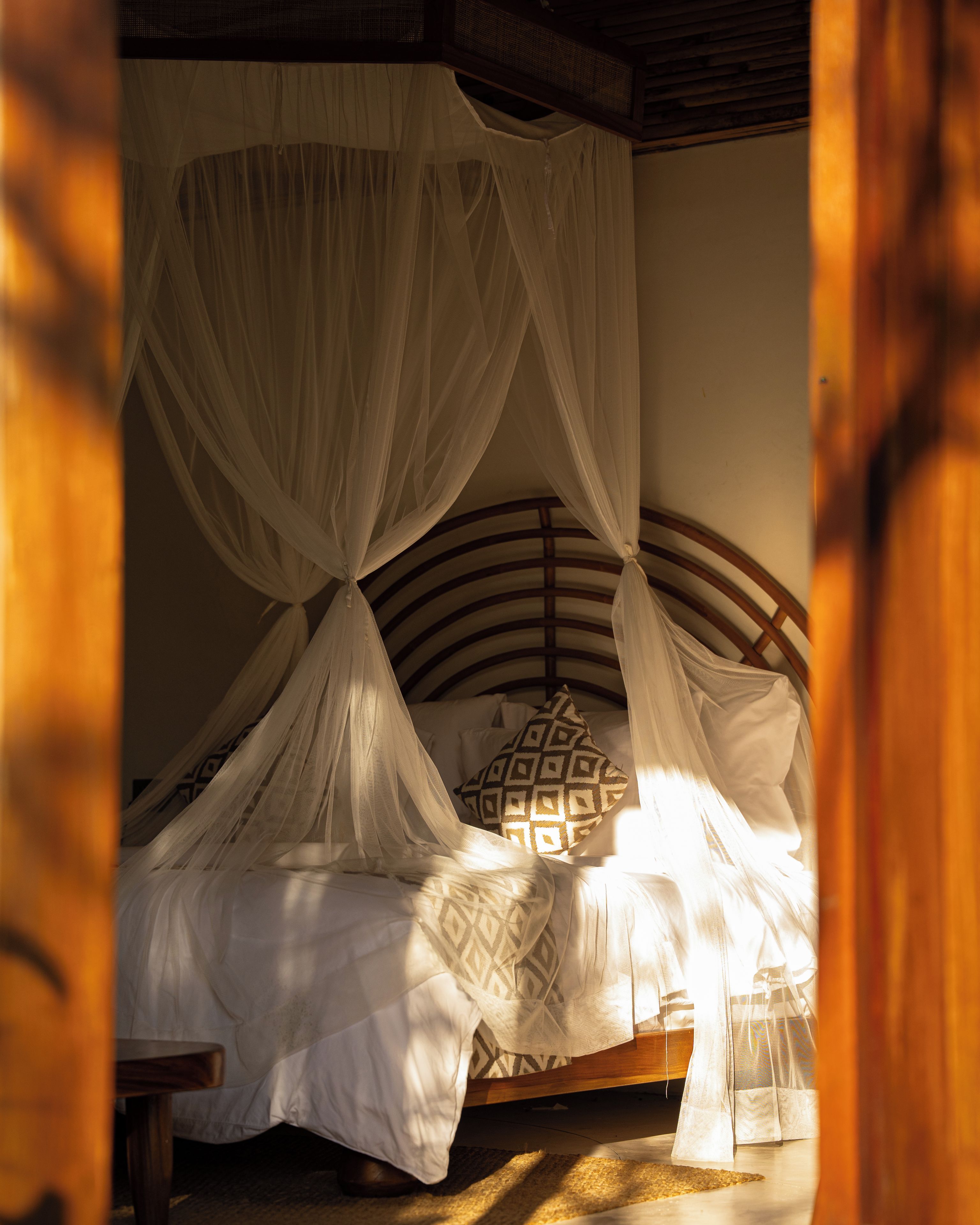 A bed with a canopy, a wooden headboard, and a patterned pillow.