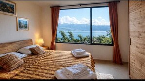 Een hotelkamer met een bed, een raam met gordijnen en lijstjes met foto’s aan de muur.
