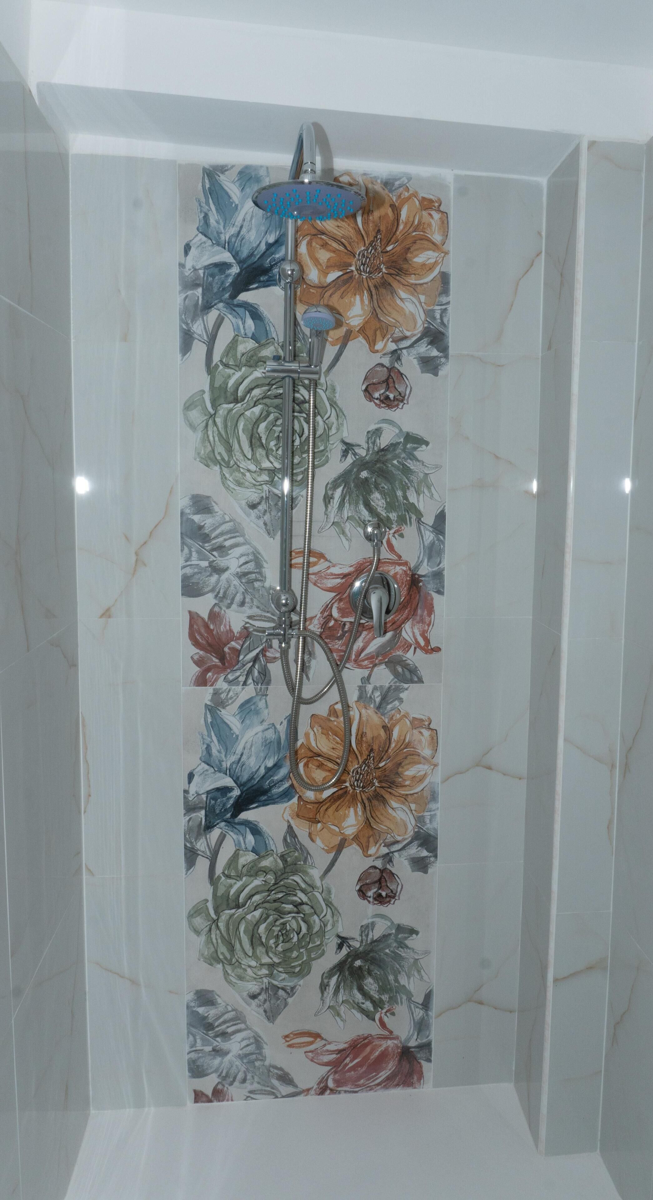 A shower with a floral tile design and a handheld showerhead.