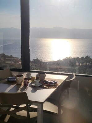 Una mesa con alimentos para el desayuno y vista al agua y montañas.