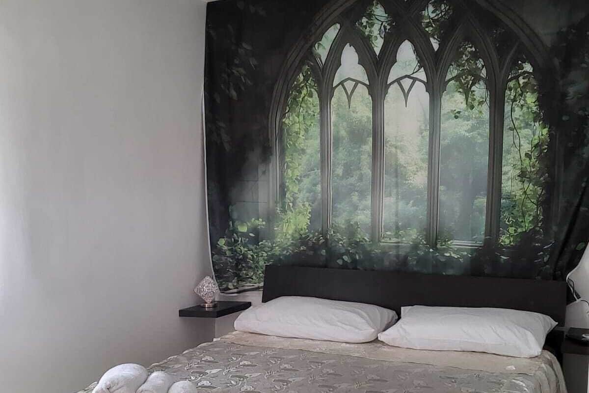A bedroom with a large bed, a gothic window mural, and a neatly made bed with towels.