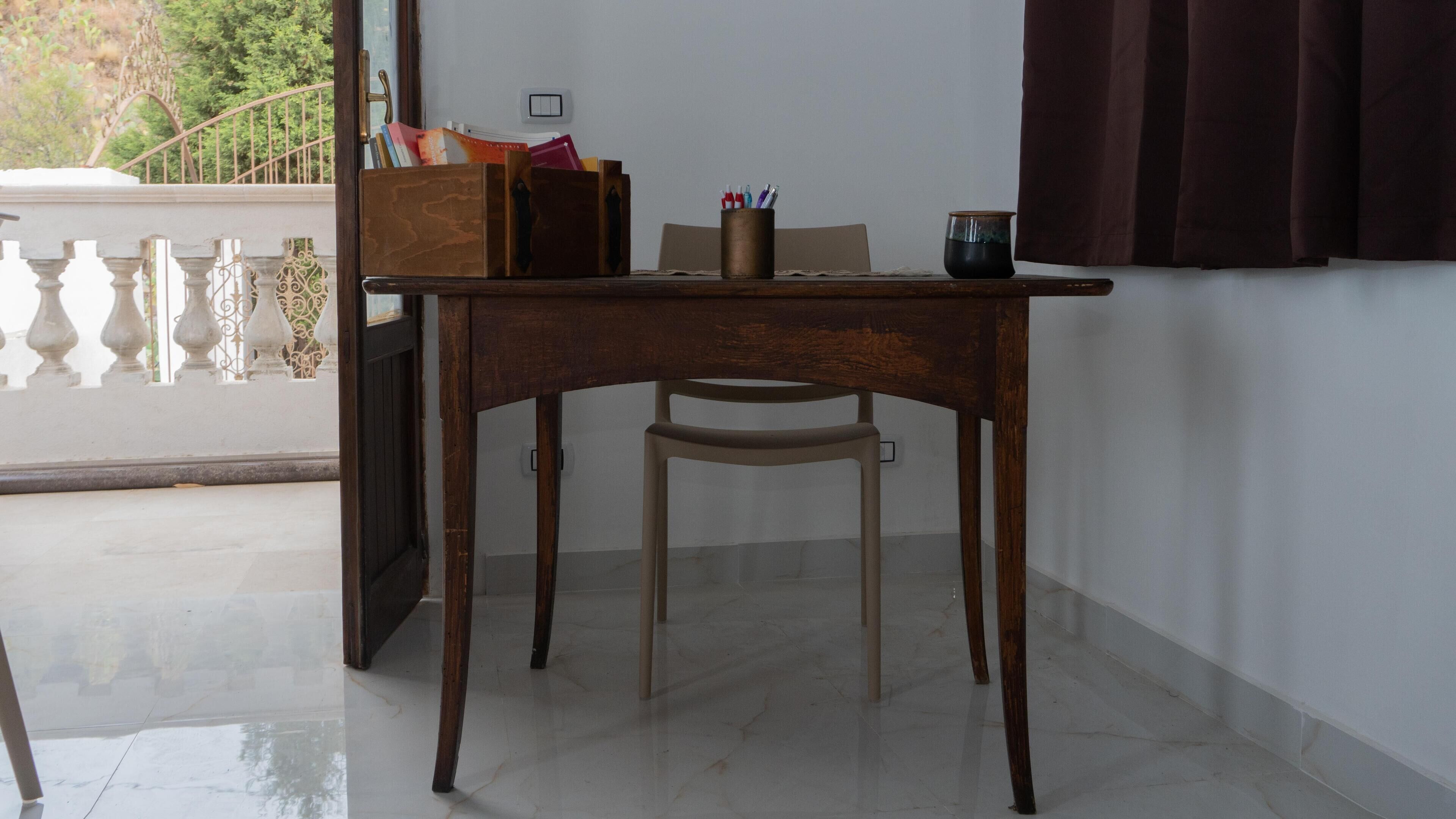 Un escritorio de madera con una silla, una mesita y una ventana con cortinas.