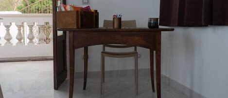 Un escritorio de madera con una silla, una mesita y una ventana con cortinas.