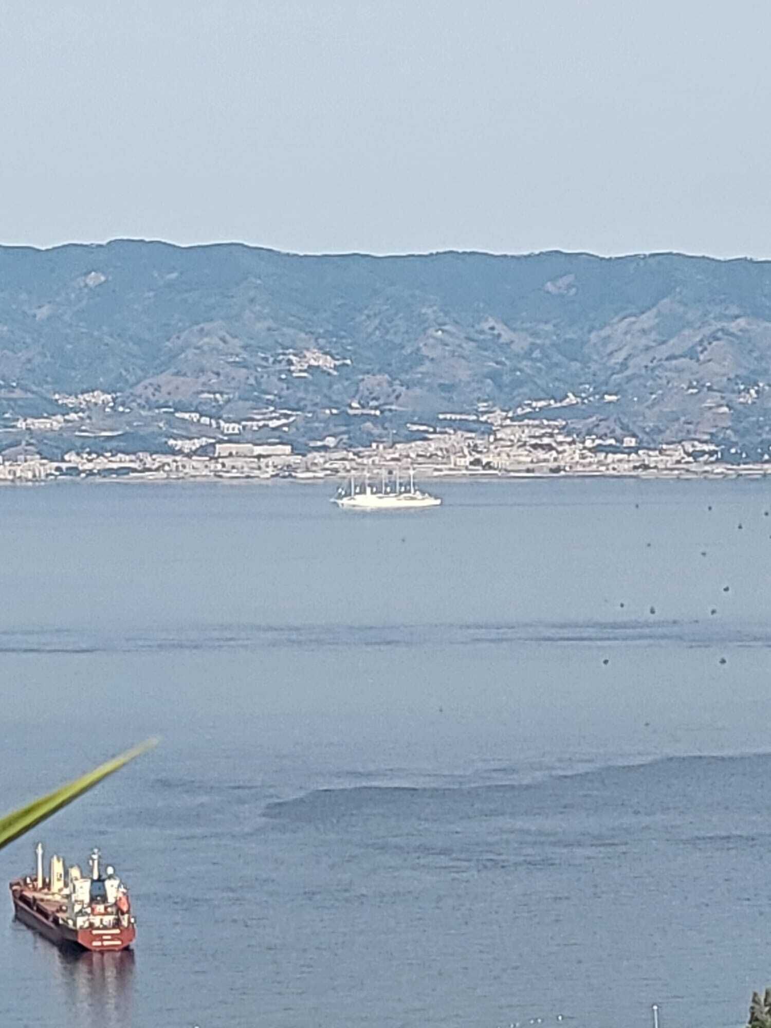 Un paisaje urbano costero con una extensa masa de agua, un ferry y un barco a lo lejos.