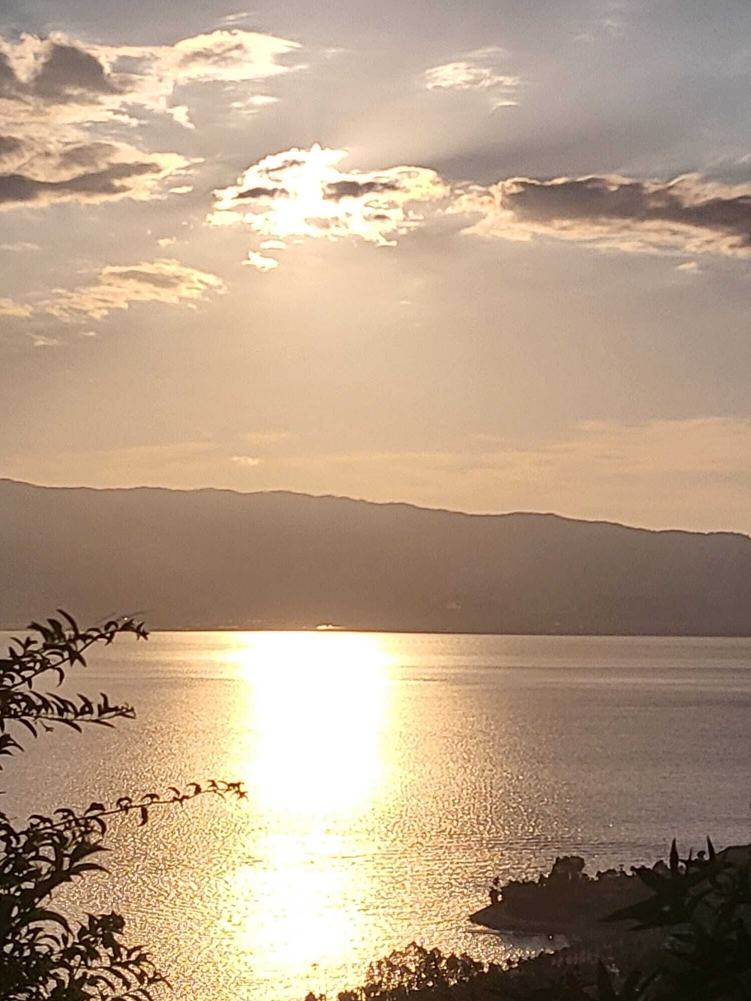 A sunset over a calm body of water with distant mountains.