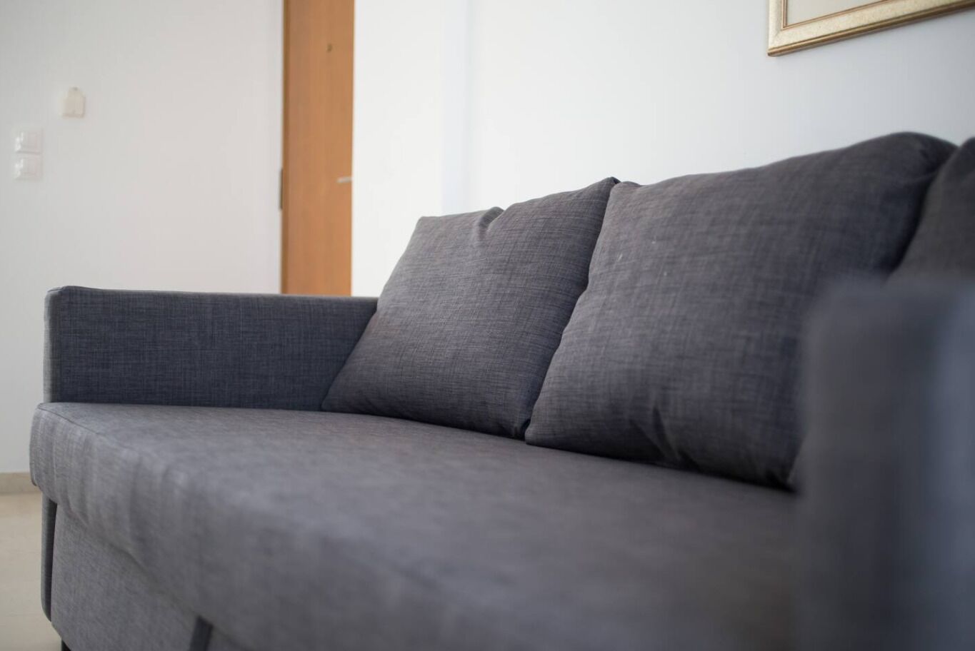 A grey sofa in a room with a wooden door and a framed picture on the wall.
