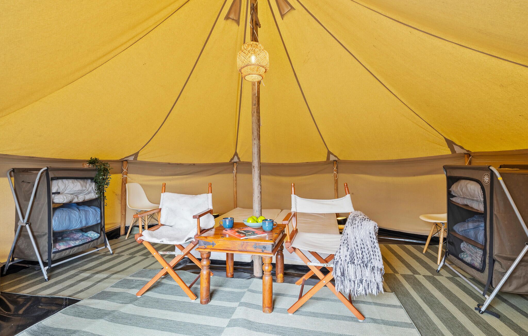 Une tente avec une table au centre, deux chaises et un luminaire suspendu.