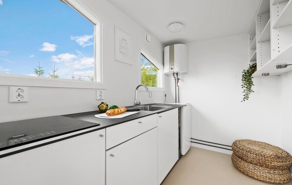 Una cocina moderna con armarios blancos, encimera negra, un fregadero y una ventana con vistas a árboles.